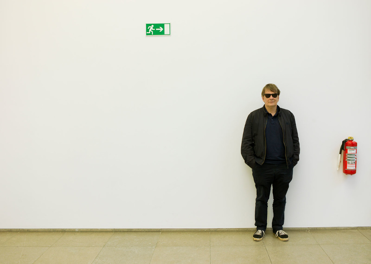 Der Autor und Musiker Sven Regener lehnt mit Sonnenbrille neben einem Feuerlöscher an der Wand.