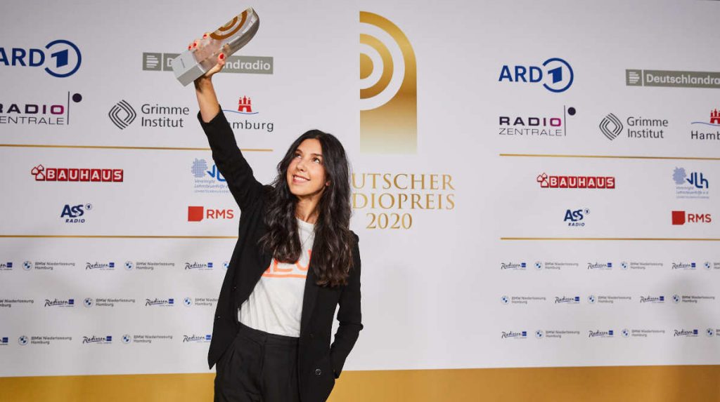 Deutscher Radiopreis 2020, das Bild zeigt Moderatorin Sandra Gern, wie sie stolz den Preis vor der Sponsorenwand zeigt