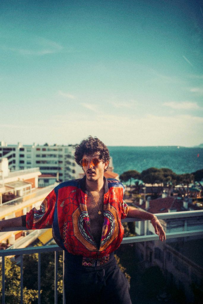 Kid Simius hosted die Radioshow Ácido Flamenco Rave Club, hier sieht man ihn vor einem spanischem Hafen an einem Geländer lehnend.