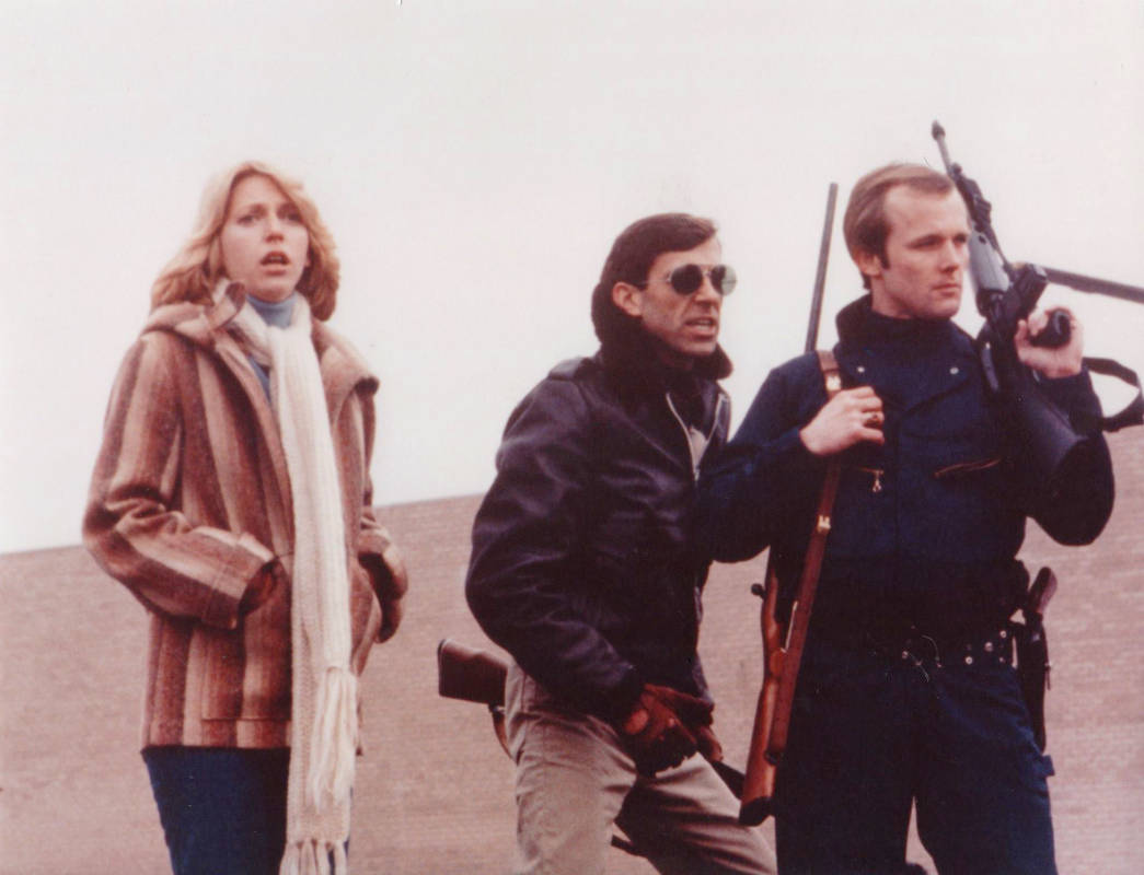 Horror Klassiker "Zombie - Dawn Of The Dead" von George A. Romero: auf diesem Szenenbild sieht man eine Frau und zwei Männer. Die Frau hat einen schockierten Gesichtsausdruck und die zwei Männer tragen Gewehre.