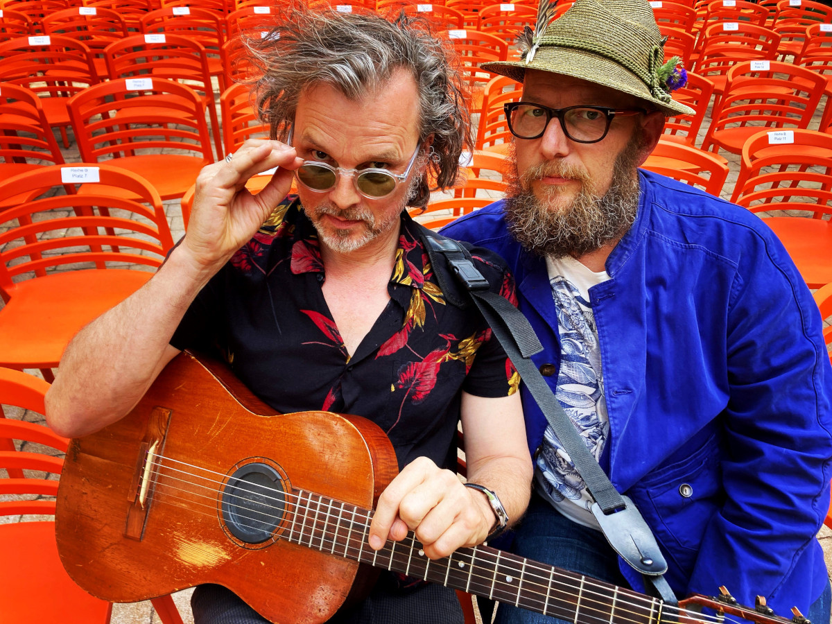 Plié - heißt das neue Album von Dreiviertellblut. Das Bild zeigt zwei Musiker vor orangen Stühlen.