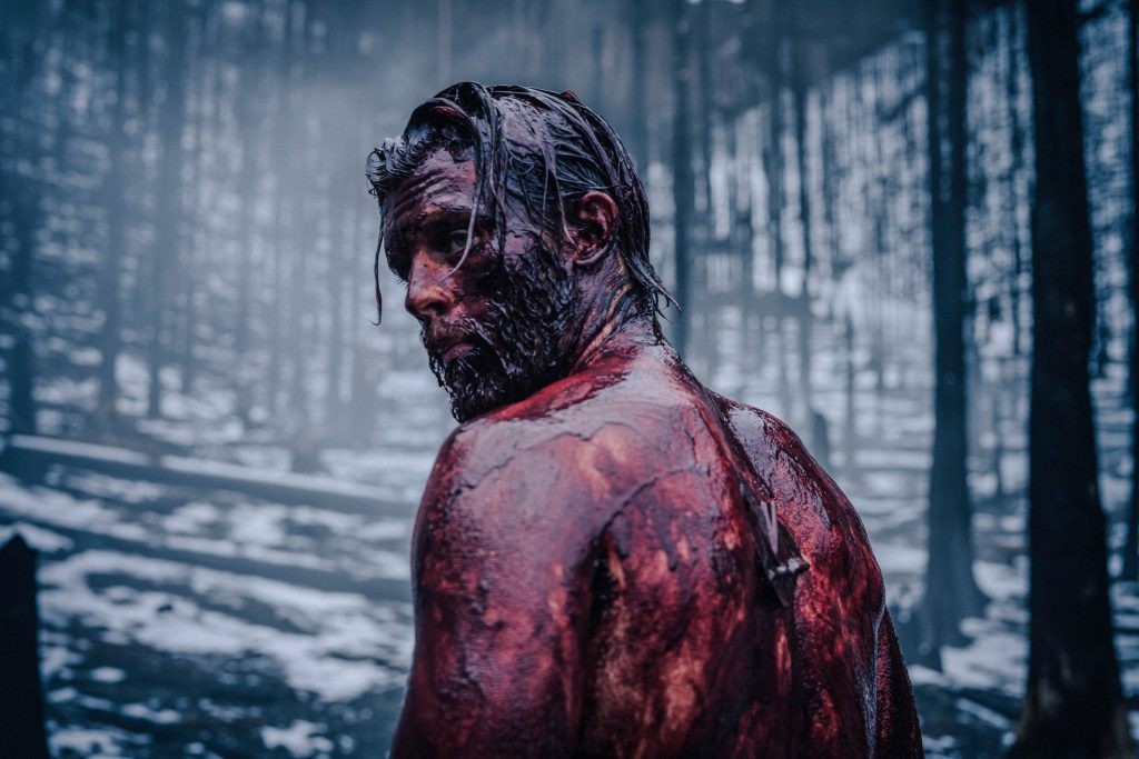 Nibelungenlied als Serie: Jannis Niewöhner als Siegfried von Xanten. Siegfried steht mit nacktem blutverschmierten Oberkörper im Wald und blickt über die Schulter.