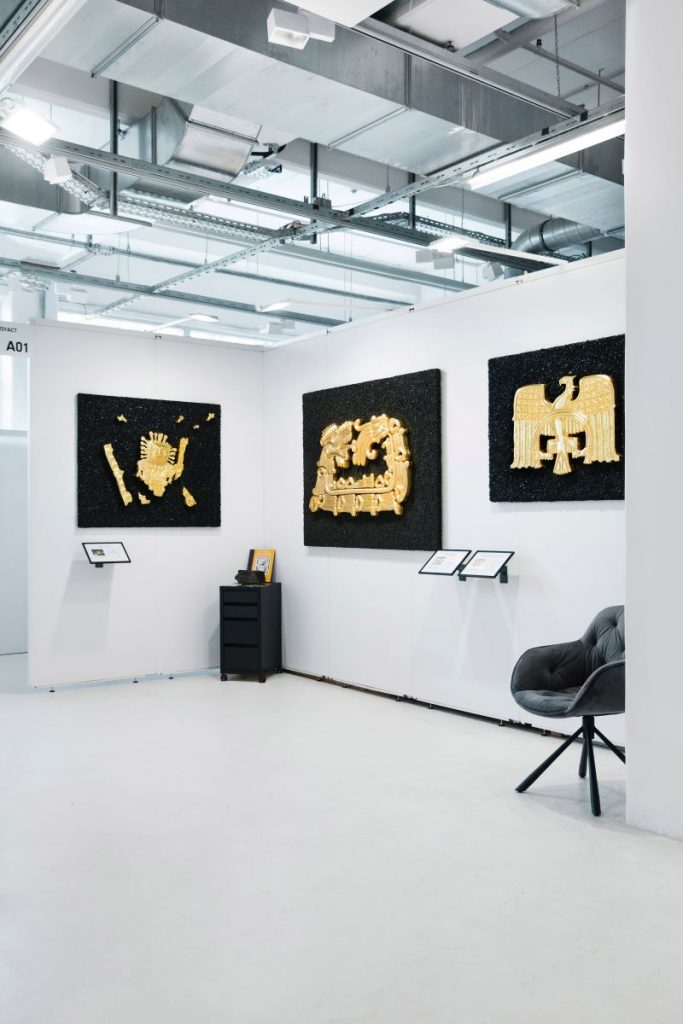 Zu sehen ist eine Ausstellungsfläche auf dem Kunstevent ARTMUC. Die ausgestellten Bilder zeigen ausschließlich goldene Figuren auf schwarzem Hintergrund.