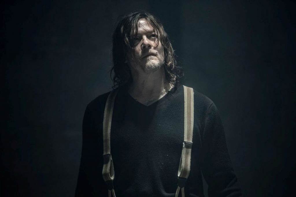 Daryl Dixon Staffel 3 - die Serie soll fortgesetzt werden. Das Bild ziegt Norman Reedus in einem schwarzen langärmligen T-Shirt und hellen Hosenträgern vor einer schwarzen Wand.
