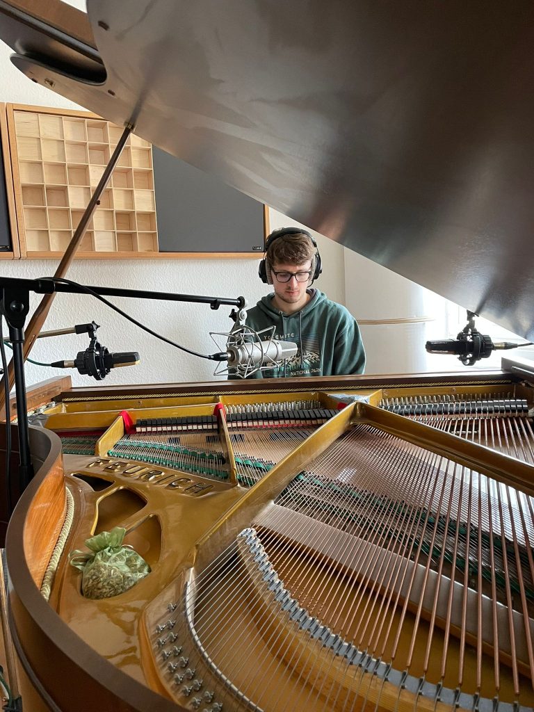 Fabian Kratzer im Aufnahmestudio: Der Musiker arbeitet konzentriert an seiner neuen Single 'Transition'. Am Flügel sitzend, mit Kopfhörern und hochwertigen Mikrofonen ausgestattet, fängt er die Magie seines Spiels ein.