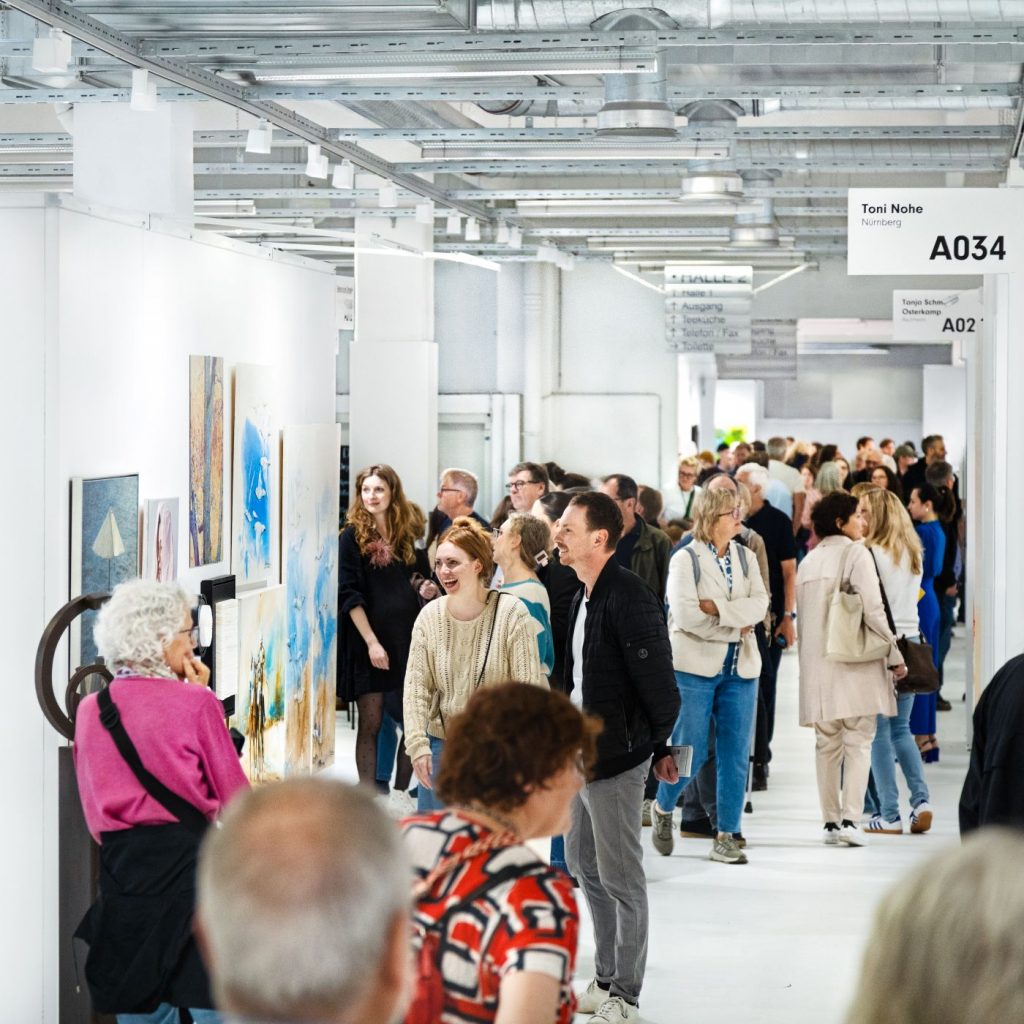 Kunstinteressierte stehen vor Exponaten auf der ARTMUC Oktober 2025 in einer hellen Ausstellungshalle.