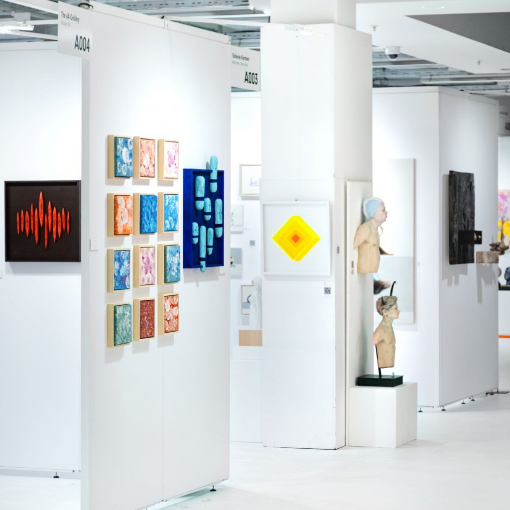Verschiedene Gemälde und Skulpturen werden in einer hellen Ausstellungshalle der ARTMUC Oktober 2025 gezeigt.