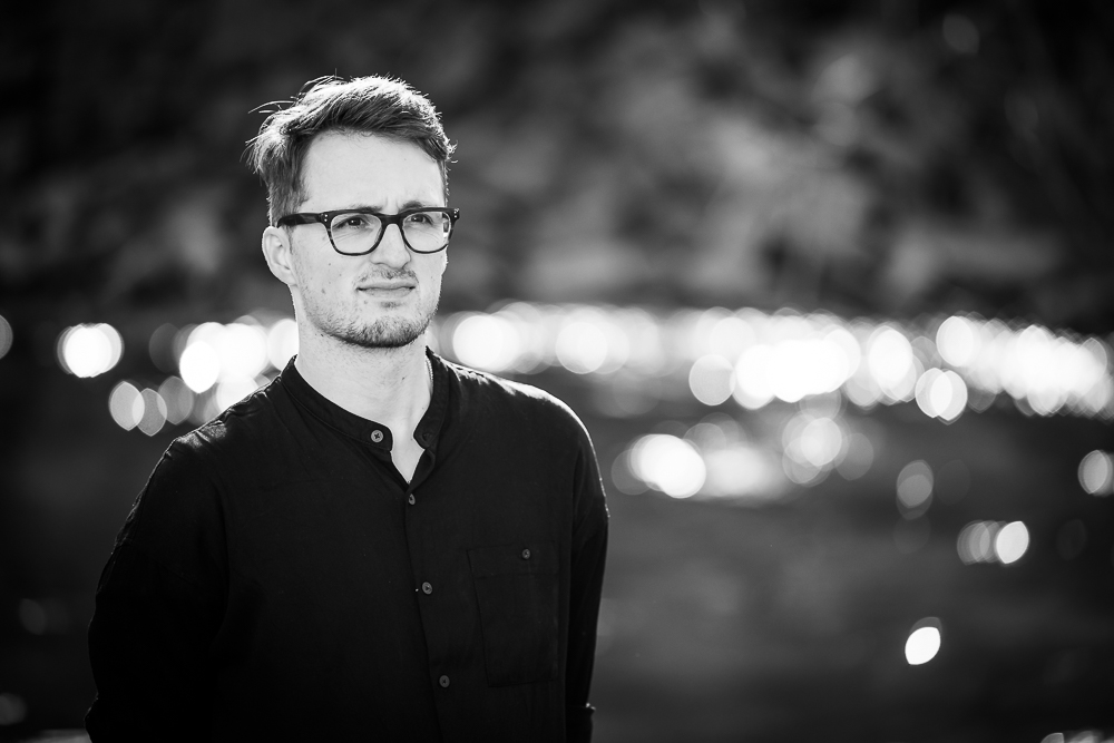 Porträt von Komponist Fabian Kratzer, aufgenommen in Schwarz-Weiß, mit unscharfen Lichtreflexen im Hintergrund.