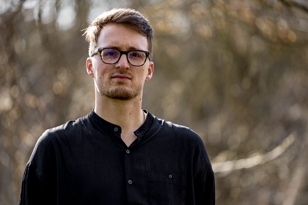 Porträt von Komponist Fabian Kratzer im Freien, mit schwarzem Hemd und unscharfem Naturhintergrund.