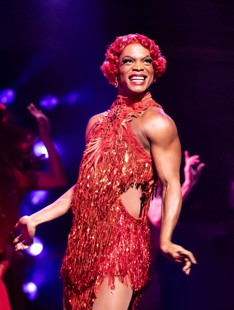 Drag Queen München in rotem Glitzerkleid auf der Bühne, Szene aus dem Musical Kinky Boots.