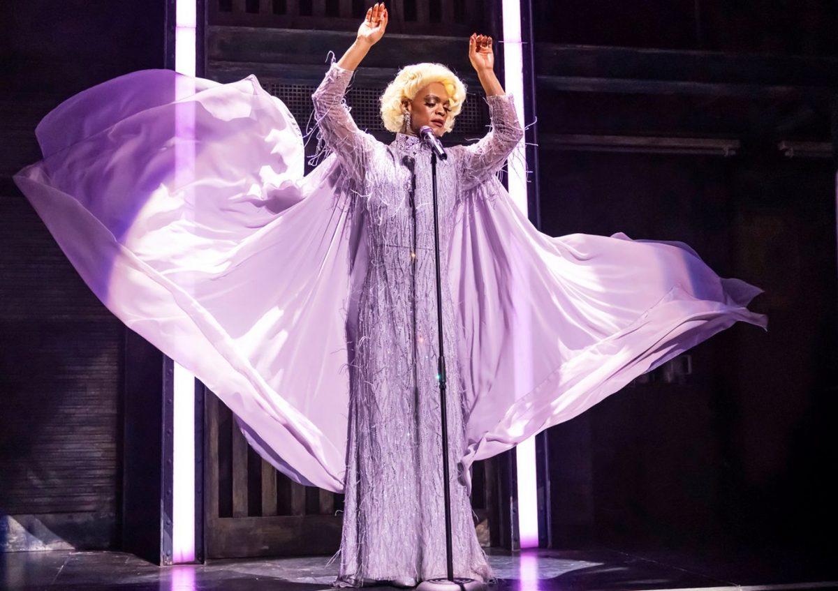 Drag Queen in lilafarbenem Kleid mit ausgebreiteten Armen, Szene aus der Kultshow München Kinky Boots.