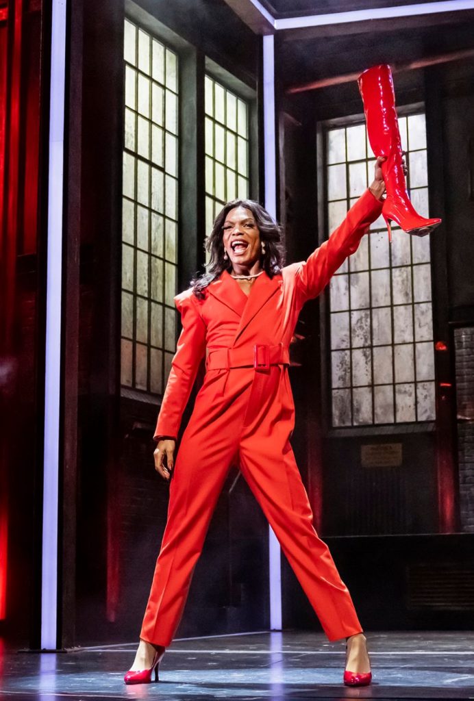 Drag Queen in rotem Anzug mit rotem Stiefel auf der Bühne, Szene aus dem Musical Kinky Boots mit Hits von Cyndi Lauper.