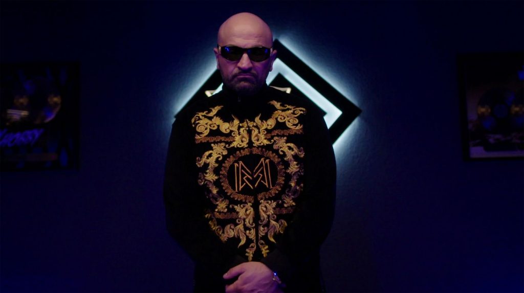 Rapper Xatar in der ARD-Doku über Rapper Xatar mit Sonnenbrille und goldverzierter Jacke in dunkler, blau beleuchteter Szene, fotografiert von Jesse Mazuch