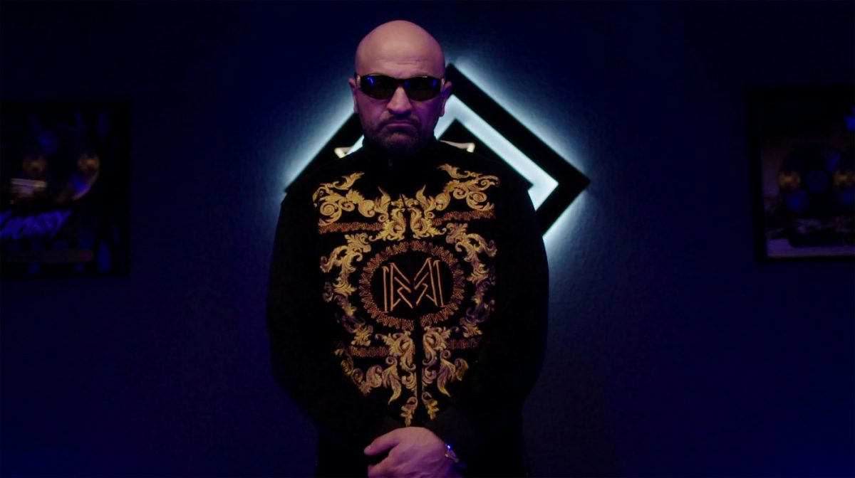 Rapper Xatar in der ARD-Doku über Rapper Xatar mit Sonnenbrille und goldverzierter Jacke in dunkler, blau beleuchteter Szene, fotografiert von Jesse Mazuch