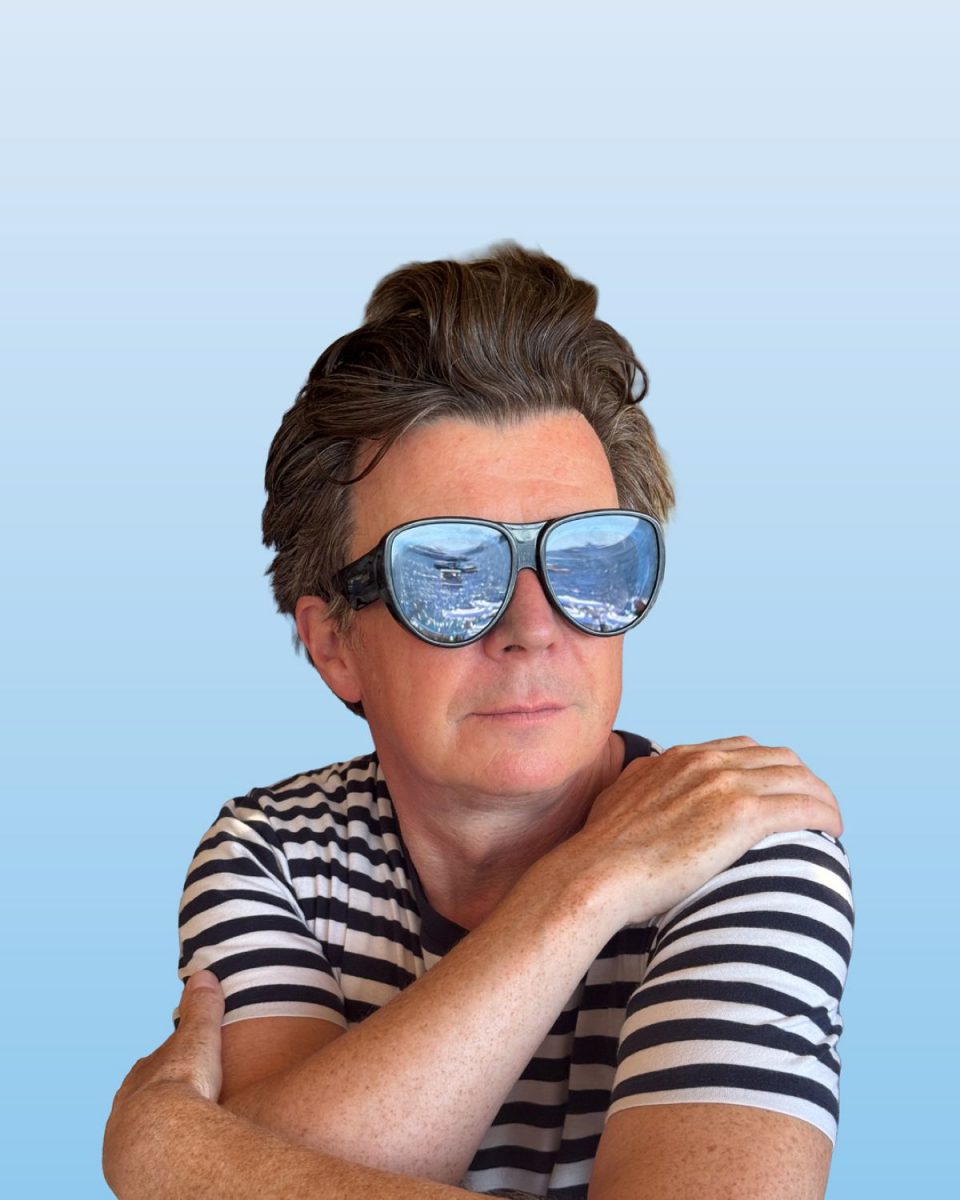 Rick Astley live Porträt mit Sonnenbrille vor blauem Hintergrund