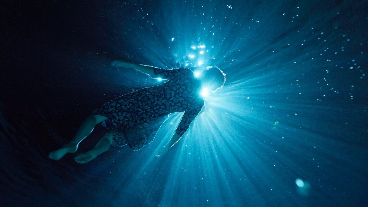Person schwebt unter Wasser vor einem hellen Lichtstrahl.